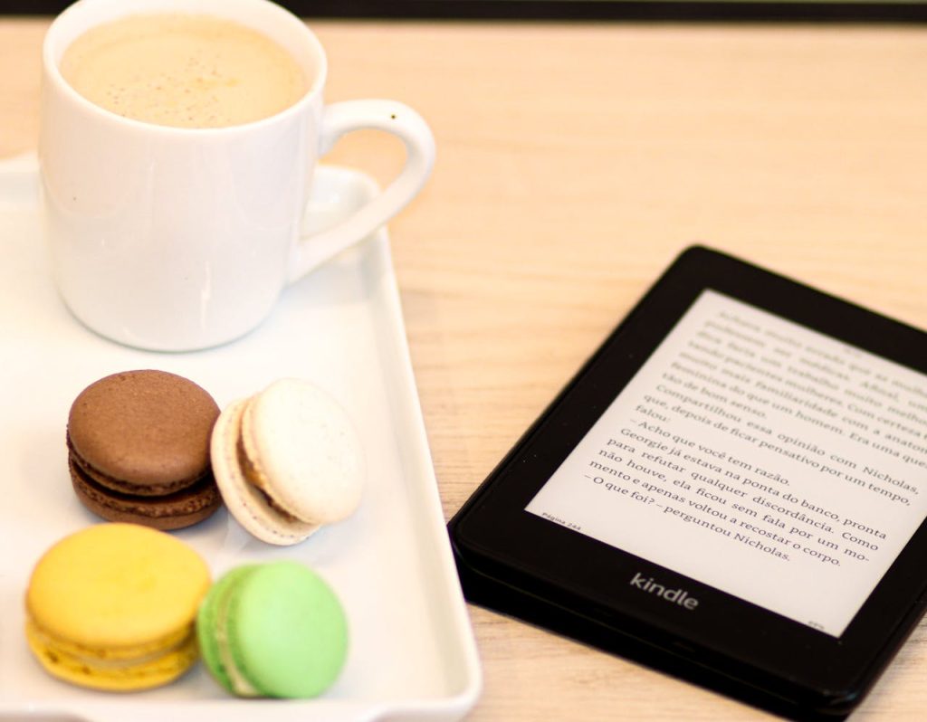 Cozy setup with coffee, colorful macarons, and Kindle e-reader on table.